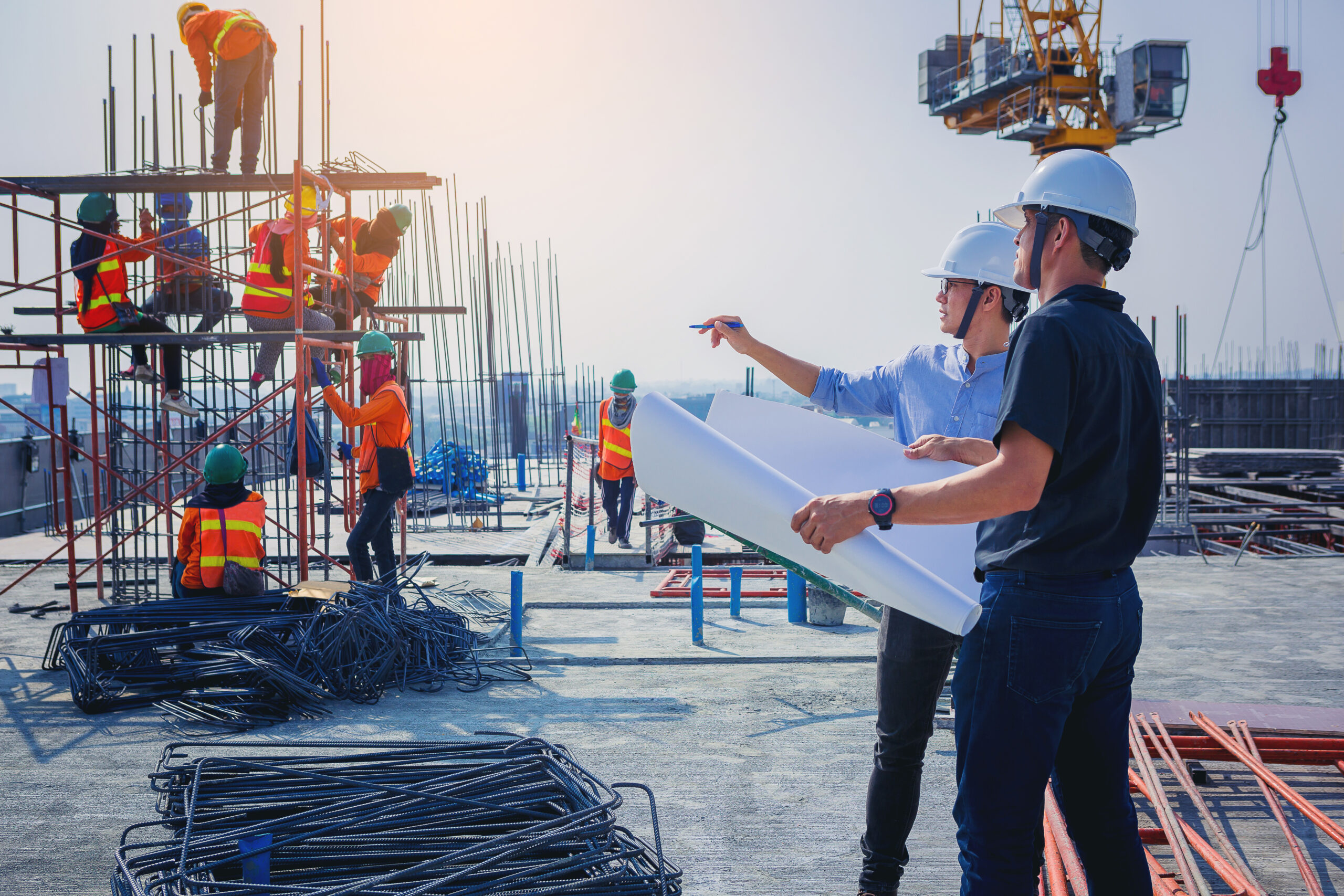 Two men in hard hats and a white shirt are standing on the construction site.